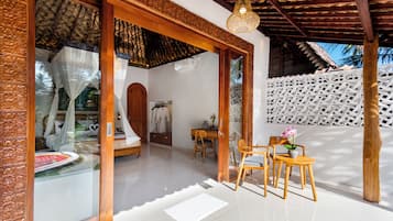 A room with a bed, a sitting area with chairs and a table, and a view of the outdoors.