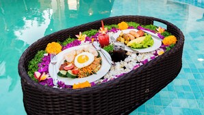 A poolside dining setup with a wicker basket containing a meal, a pool, and a building with a tiled roof in the background.