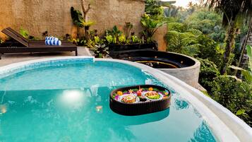 A swimming pool with a floating basket of food, lounge chairs, and tropical plants.