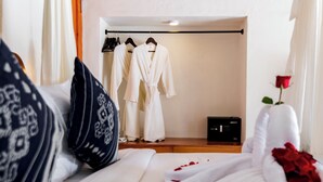A hotel room with a bed, a robe, a set of towels, and a rose.