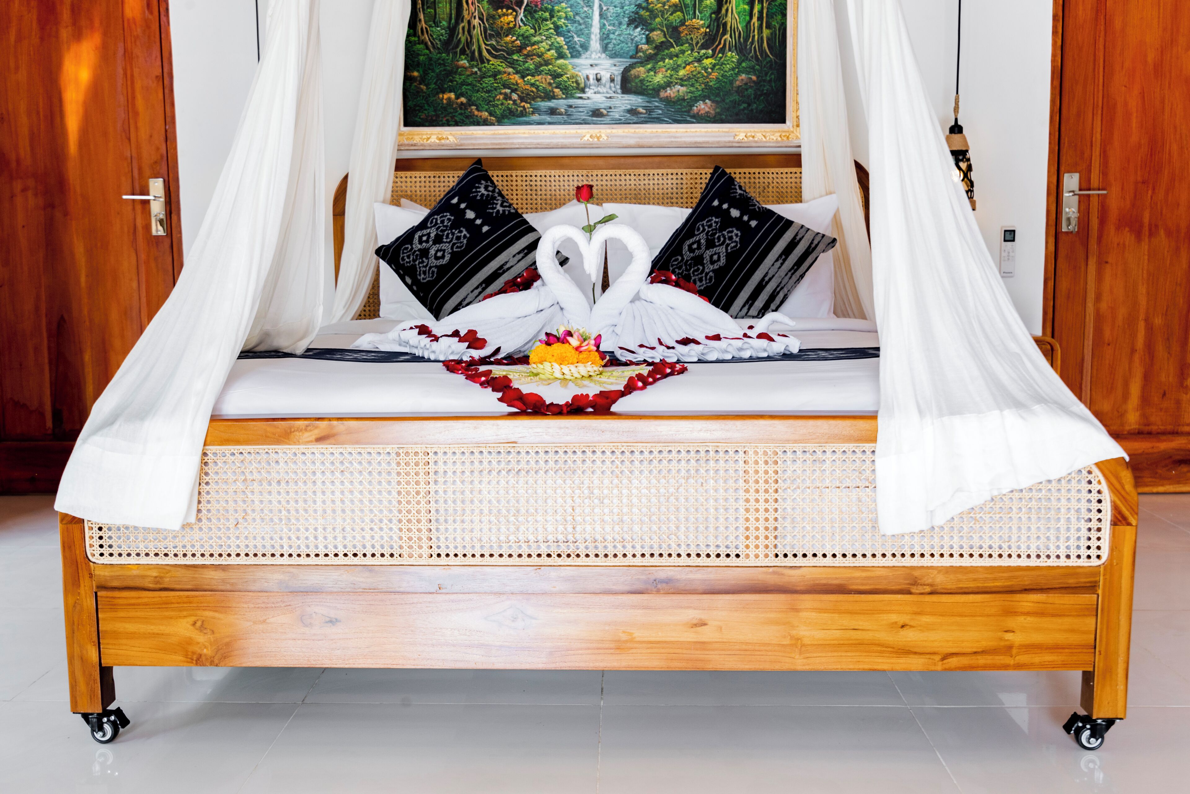 A bed with a canopy, a swan-shaped towel arrangement, and a painting of a waterfall.