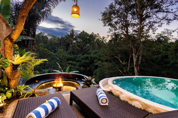 A poolside area with lounge chairs and a hot tub, surrounded by lush greenery.