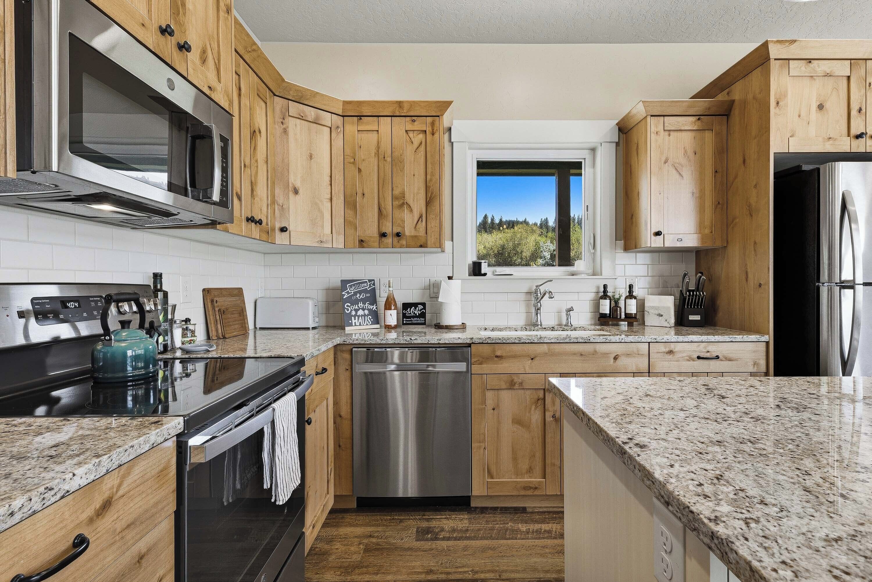 A modern kitchen with wooden cabinets, stainless steel appliances, a dishwasher, and a window with a view.