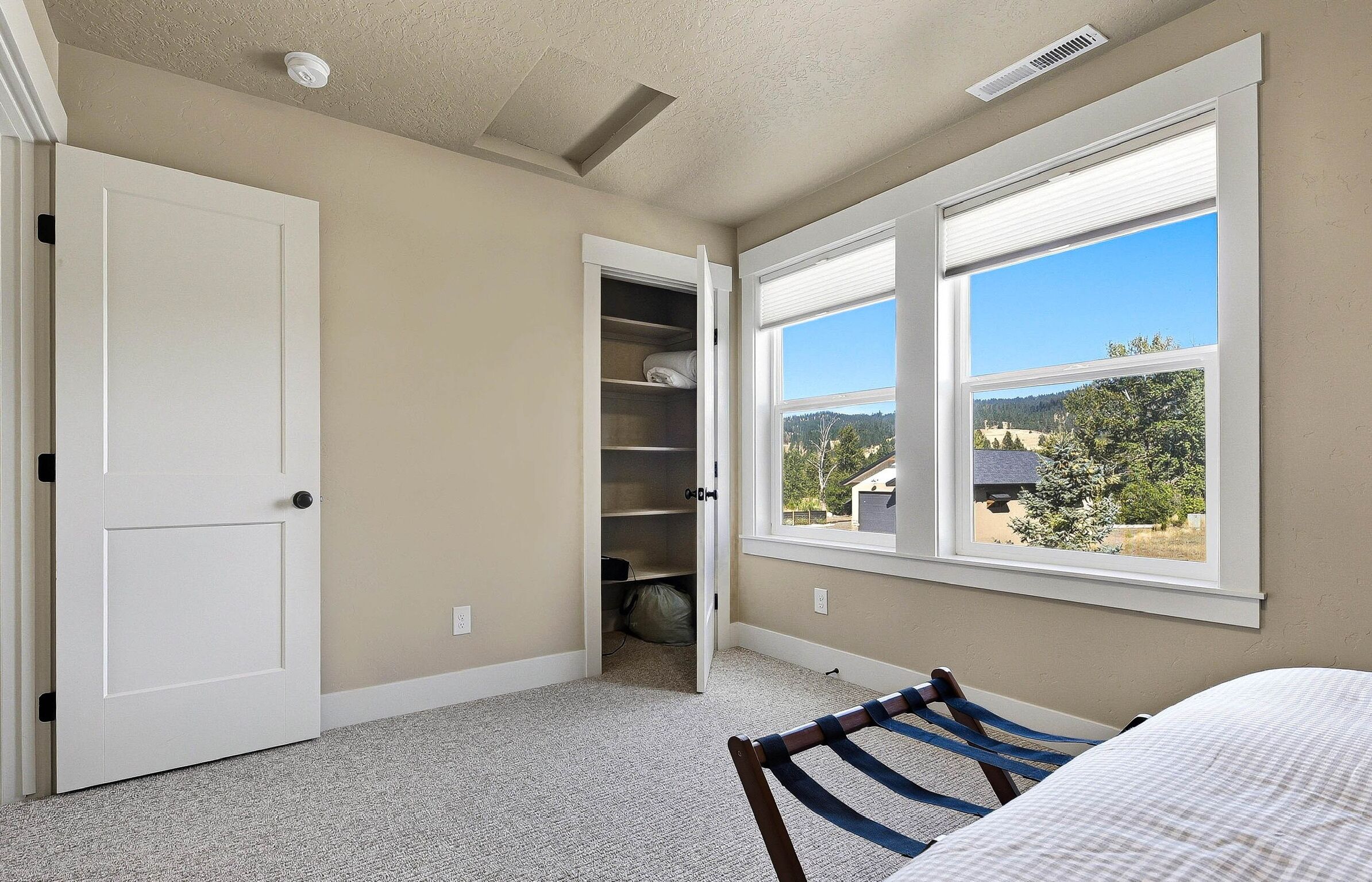A bedroom with a bed, a window with a view, a closet, and a door.
