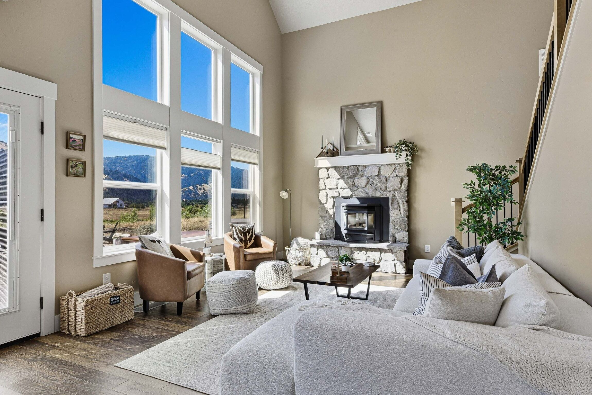 A spacious living room with a stone fireplace, large windows, and a view of the outdoors.
