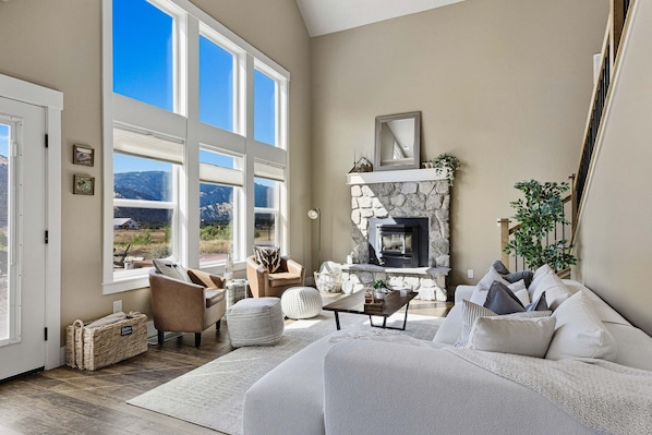 A spacious living room with a stone fireplace, large windows, and a view of the outdoors.
