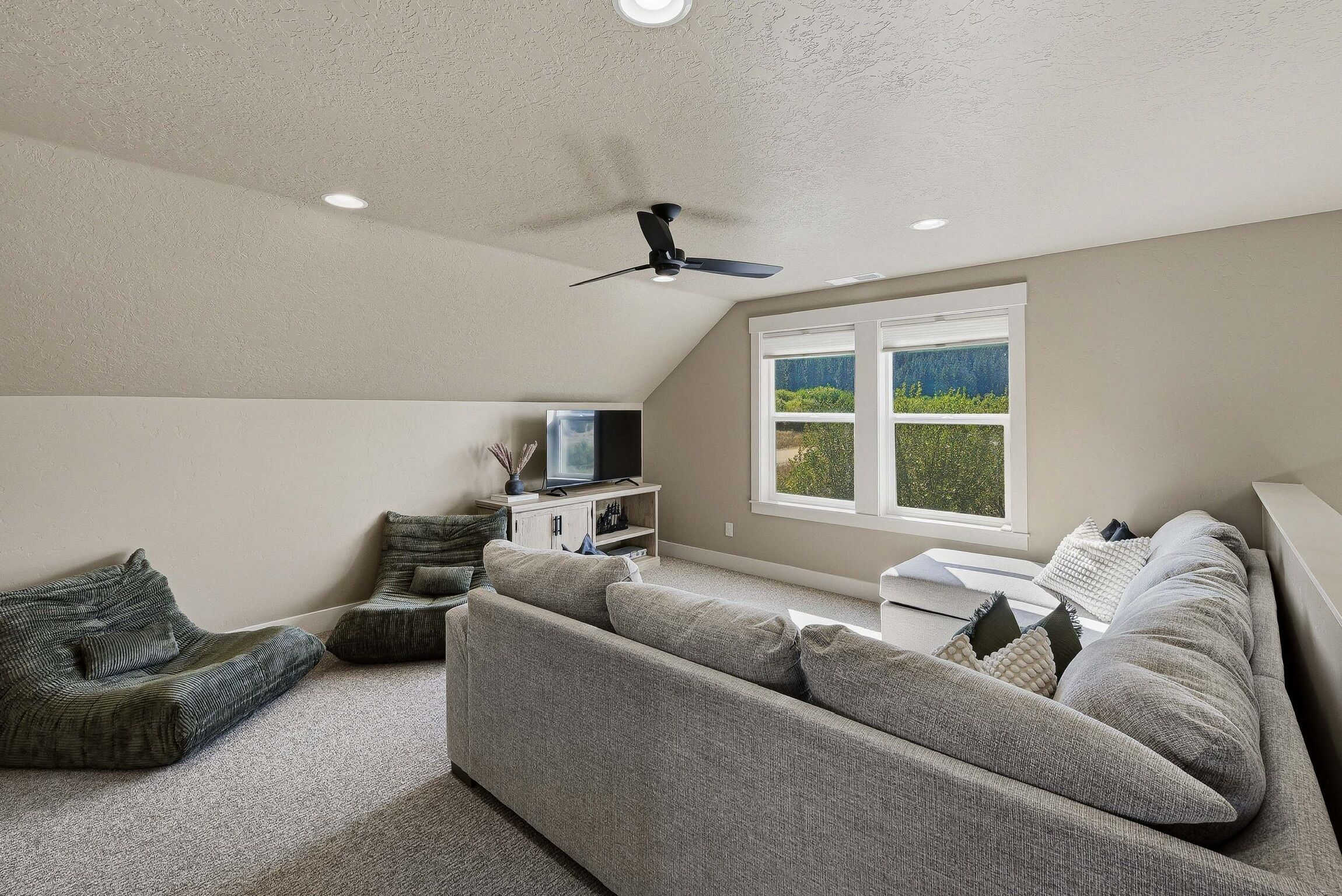 Un salon moderne avec un canapé gris, un téléviseur et un ventilateur de plafond.