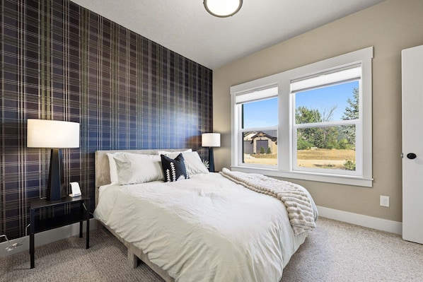 A bedroom with a bed, two bedside tables, two lamps, a window with a view, and a wall with a plaid pattern.