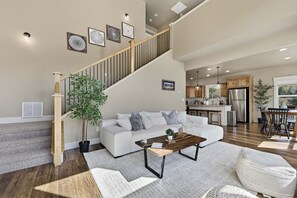 A spacious living room with a staircase, a dining area, and a kitchen with wooden cabinets.
