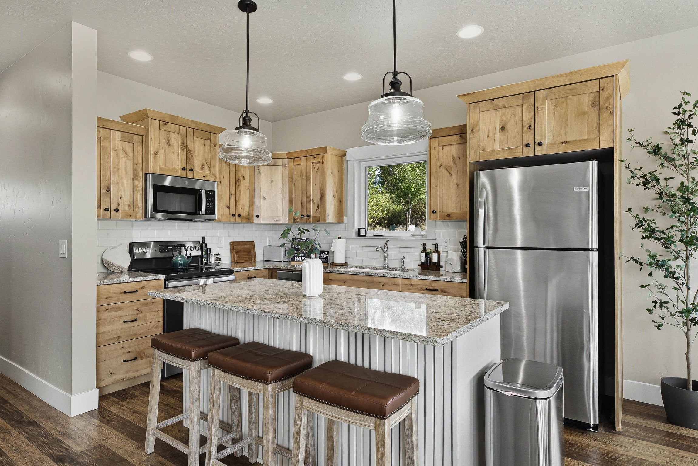 A modern kitchen with wooden cabinets, stainless steel appliances, a granite countertop, and a bar stool area.