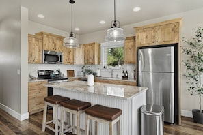 A modern kitchen with wooden cabinets, stainless steel appliances, a granite countertop, and a bar stool area.