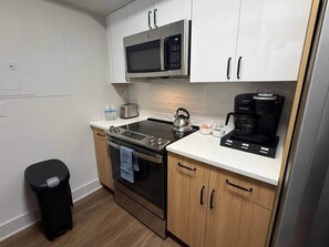 Una cocina compacta con microondas, hervidor, cafetera y tostadora.