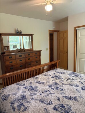 A bedroom with a wooden dresser, a bed with a blue and white patterned bedspread, and a ceiling fan. - Charming 2-bedroom house near Clearwater Lake and the Black River (Piedmont)