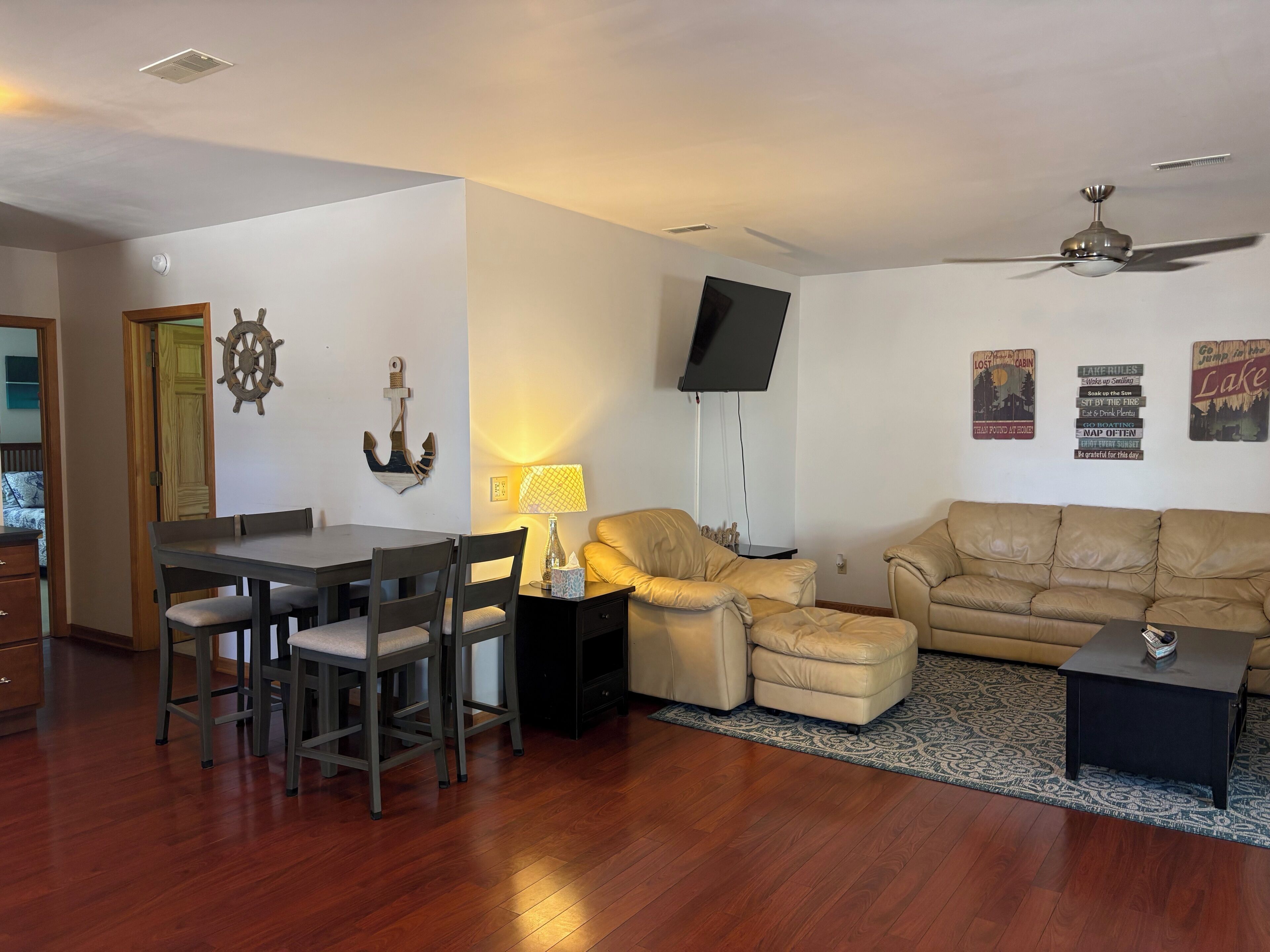A living room with a dining area, a flat-screen TV, and a ceiling fan.