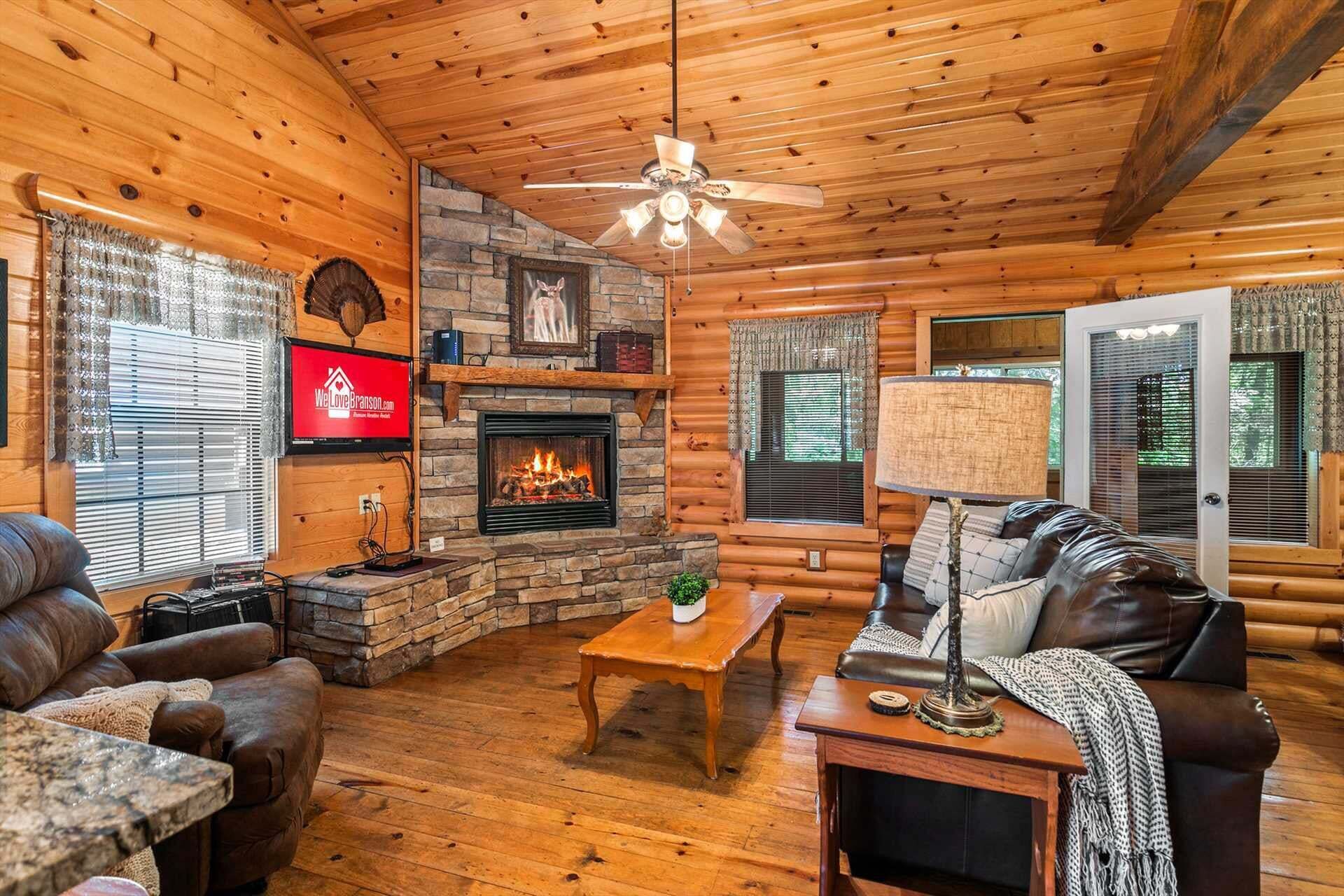 Ein gemütliches Blockhaus-Interieur mit Kamin aus Stein, Ledermöbeln und einem an der Wand montierten Fernseher.