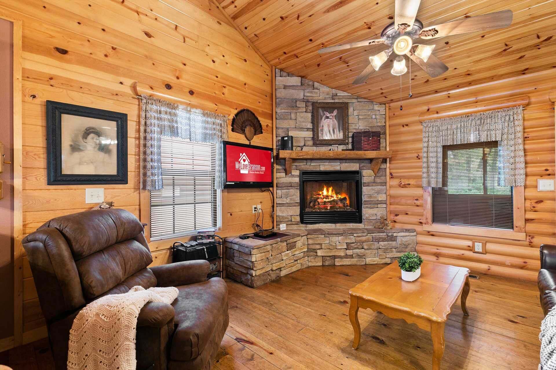 Un acogedor interior de cabaña de madera con chimenea, sofá de cuero y ventilador de techo.