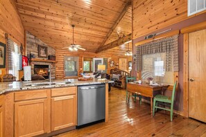 A log cabin interior with a kitchen area, dining space, and a fireplace. - Cabin with WhirlpoolTub, Free Attraction Tickets, Fireplace and Gated Community! (Branson)
