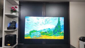 Ein Flachbildfernseher an einer dunklen Wand befestigt, mit einem Regal links, das dekorative Gegenstände beherbergt.
