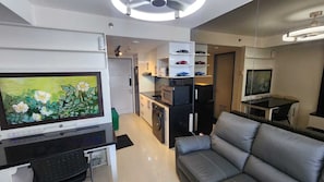 Ein modernes Wohnzimmer mit Flachbildfernseher, einer Couch und einer Küchenzeile inklusive Mikrowelle und Schränken.