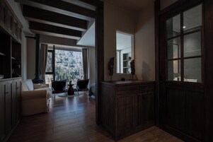 Quarto com piso de madeira, sofá branco, armário de madeira e uma janela grande com vista para uma área arborizada.