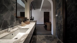 Un baño moderno con un espejo grande, un lavabo de mármol y una pared decorativa de piedra.