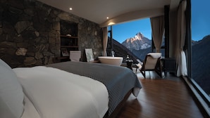 Un dormitorio con una cama grande, una pared de piedra, un baño y vistas a la montaña.