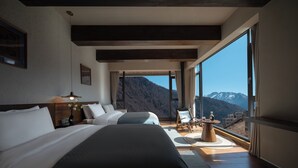 A hotel room with a large bed, a desk, a chair, and a view of mountains.