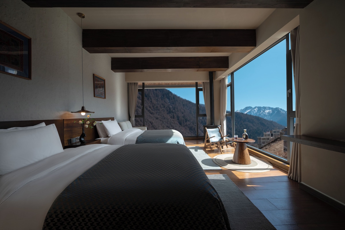 A hotel room with a large bed, a desk, a chair, and a view of mountains.