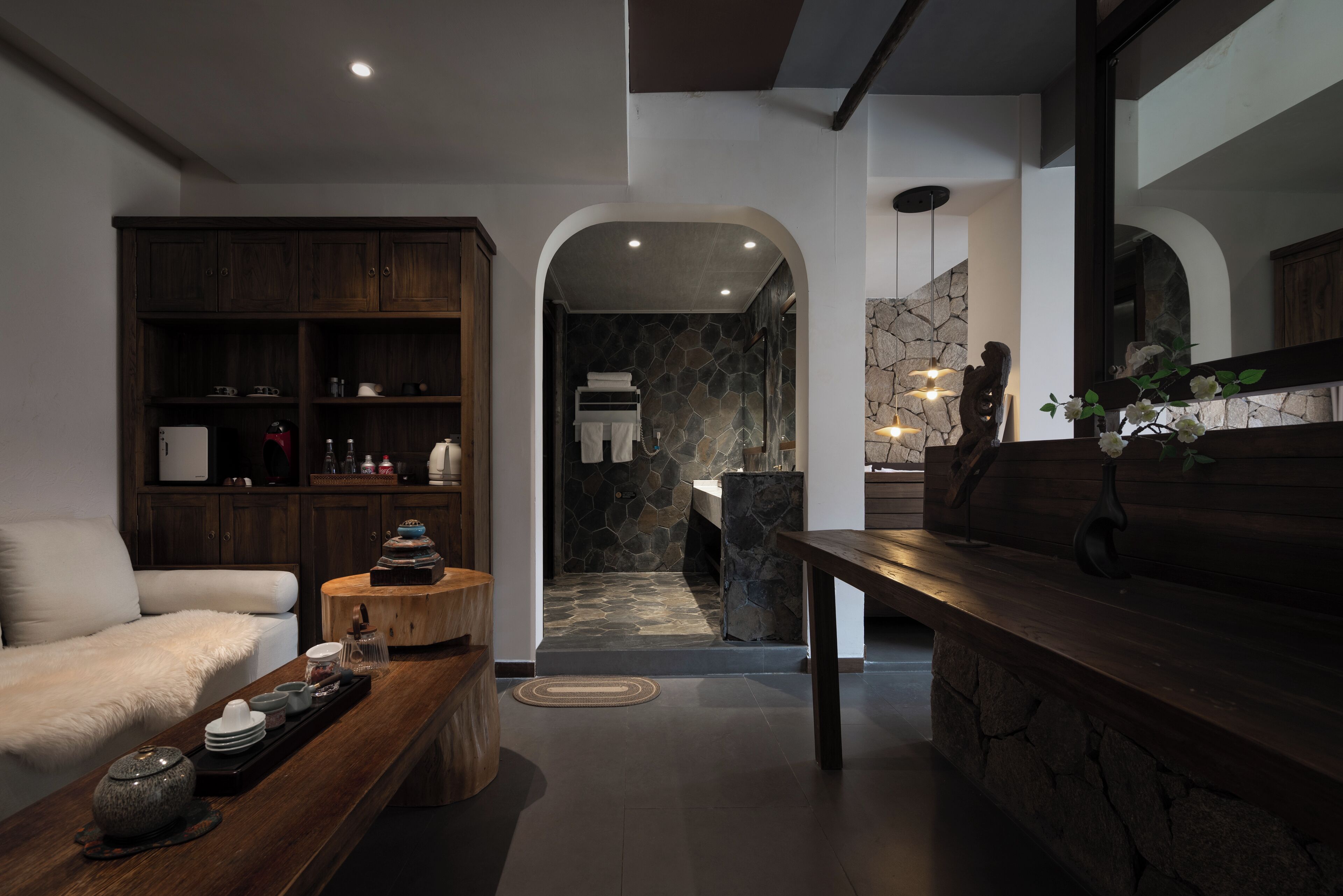 A modern interior with a wooden cabinet, a white sofa, a coffee table with dishes, and a stone wall.