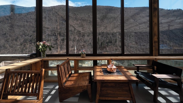 A wooden table and chairs with a view of a mountainous landscape through large windows.