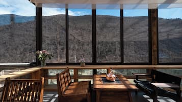 A wooden table and chairs with a view of a mountainous landscape through large windows.