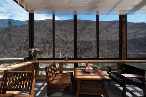 Une table et des chaises en bois, avec vue sur un paysage montagneux grâce à de grandes fenêtres.
