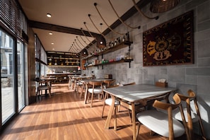 A restaurant interior with wooden tables and chairs, a kitchen area, and a large decorative wall piece. - Yueshan Four Seasons Homestay (Ngawa Autonomous Prefecture)
