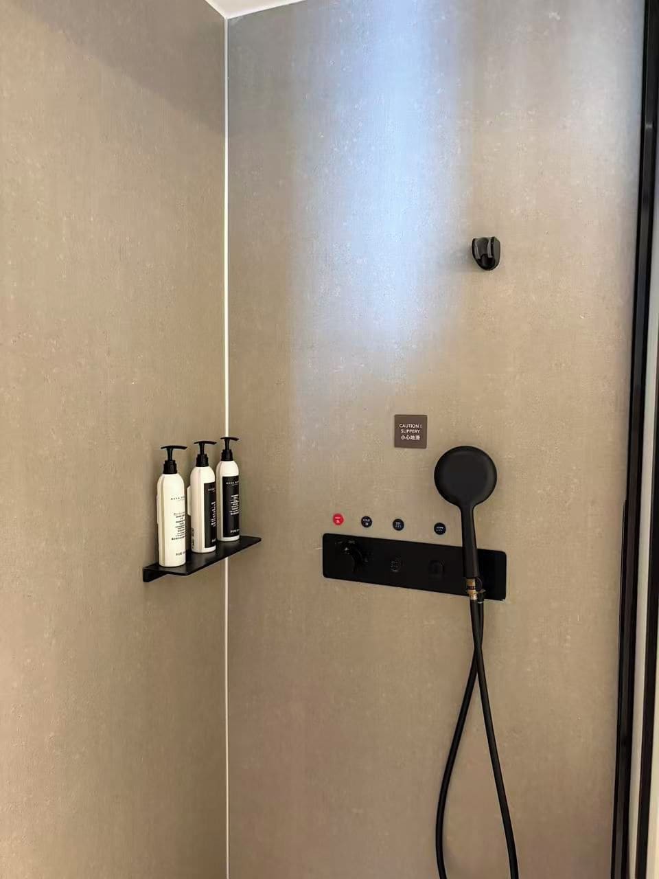 Un espace douche équipé d’un panneau de commande, d’une étagère pour les articles de toilette et d’un panneau d’avertissement.