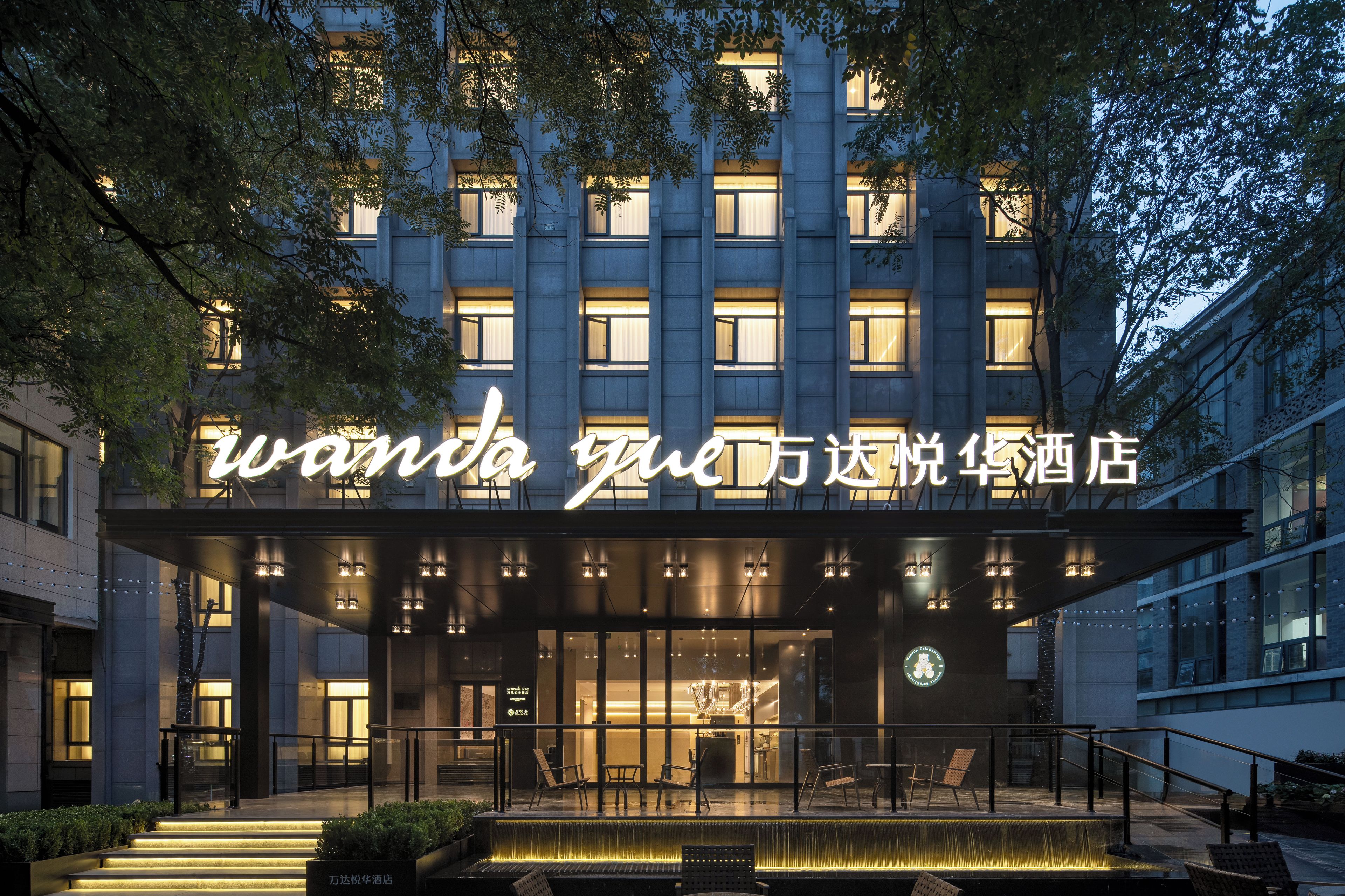 L’entrée d’un hôtel, avec une enseigne lumineuse, des places assises en plein air et un élément décoratif aquatique.
