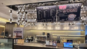 Bancada de café com um quadro de menu, máquinas de café expresso e uma tela digital exibindo o menu.