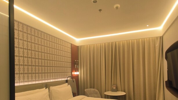 Quarto de hotel com uma cama grande, uma mesinha, uma televisão e uma parede com padrão quadriculado.