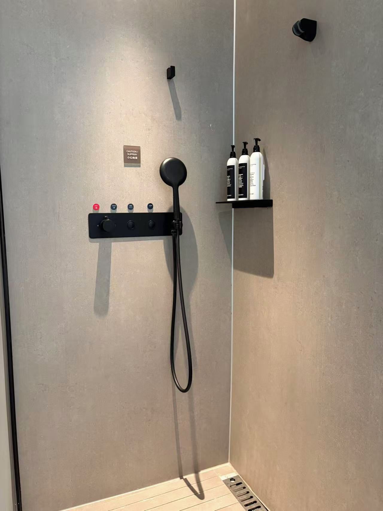 A shower area with a handheld showerhead, a control panel with multiple buttons, and a shelf with toiletries.