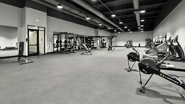 Een fitnessruimte met diverse trainingsapparaten, waaronder krachtapparaten, loopbanden en hometrainers.