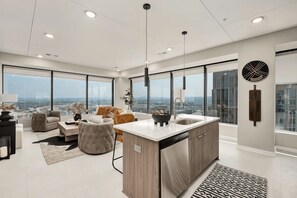Eine moderne Küche mit einer großen Kochinsel, einem Essbereich mit einer Couch und Stühlen sowie einem Blick auf die Stadt durch große Fenster.