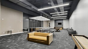 Ein moderner Lounge-Bereich mit einer Couch, einem Billardtisch und einem langen Tisch, mit hoher Decke und freiliegenden Leitungen sowie eingelassener Beleuchtung.