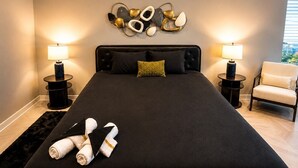 Ein Hotelzimmer mit einem großen Bett, zwei Nachttischlampen, einem Wandbild, einem Sessel und einem schwarzen Teppich.