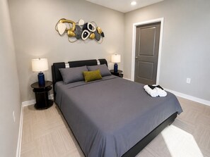 Ein modernes Schlafzimmer mit einem großen Bett, zwei Nachttischen mit Lampen, einem Wanddekor und einer Tür.