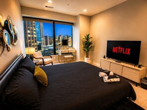Ein Hotelzimmer mit einem großen Bett, einem Schreibtisch, einem Sessel, einem Fernseher und Blick auf die Stadt.