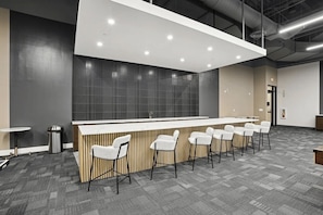 A modern bar area with a long counter and multiple bar stools. - Skyline Luxury | 2BR + King | Downtown BHM (Birmingham)