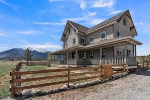 A two-story house with a porch, a fenced yard, and mountains in the background. - Beautiful Ranch with Hot Tub Near Mt.Princeton Hot Springs (Nathrop)