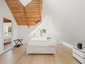 A bedroom with a sloped ceiling, a bed with white bedding, a small table, and a nightstand with a lamp. - Bass Lake/Game Room/Sleeps 22/Boat Slip (Bass Lake)