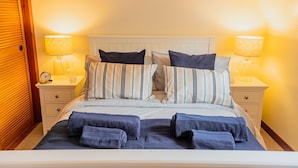 A neatly made bed with striped bedding and multiple pillows, flanked by bedside tables with lamps and a clock.