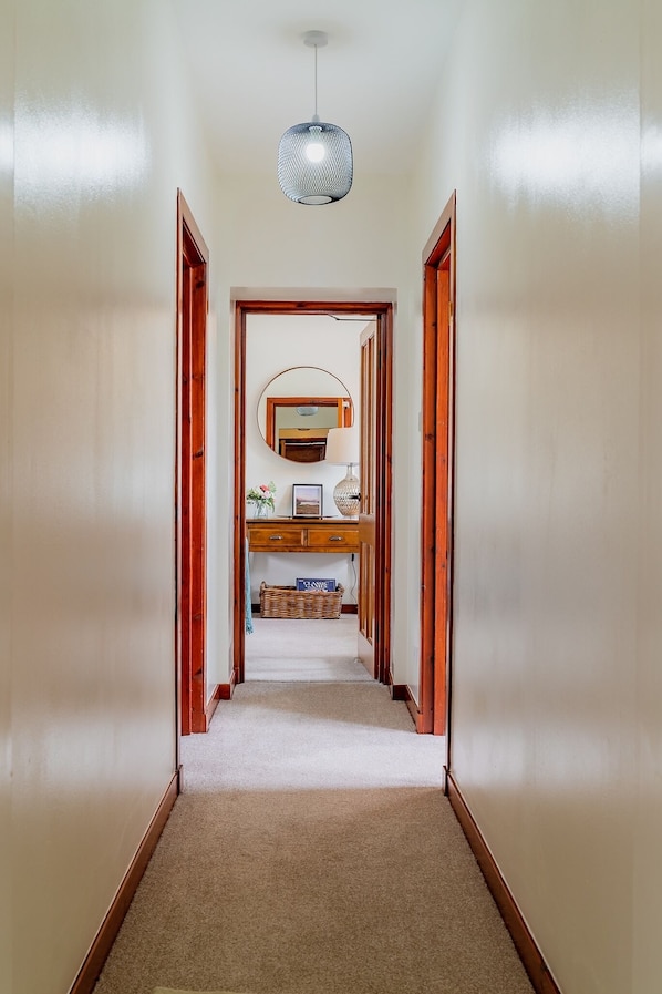 A hallway with a wooden door frame, a hanging light fixture, a mirror, and a small table with a lamp.
