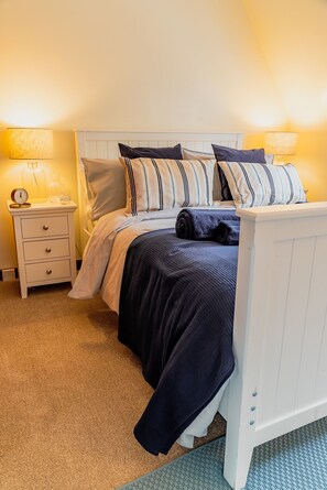A neatly made bed with striped bedding, a bedside table with a lamp, and a nightstand with a clock.